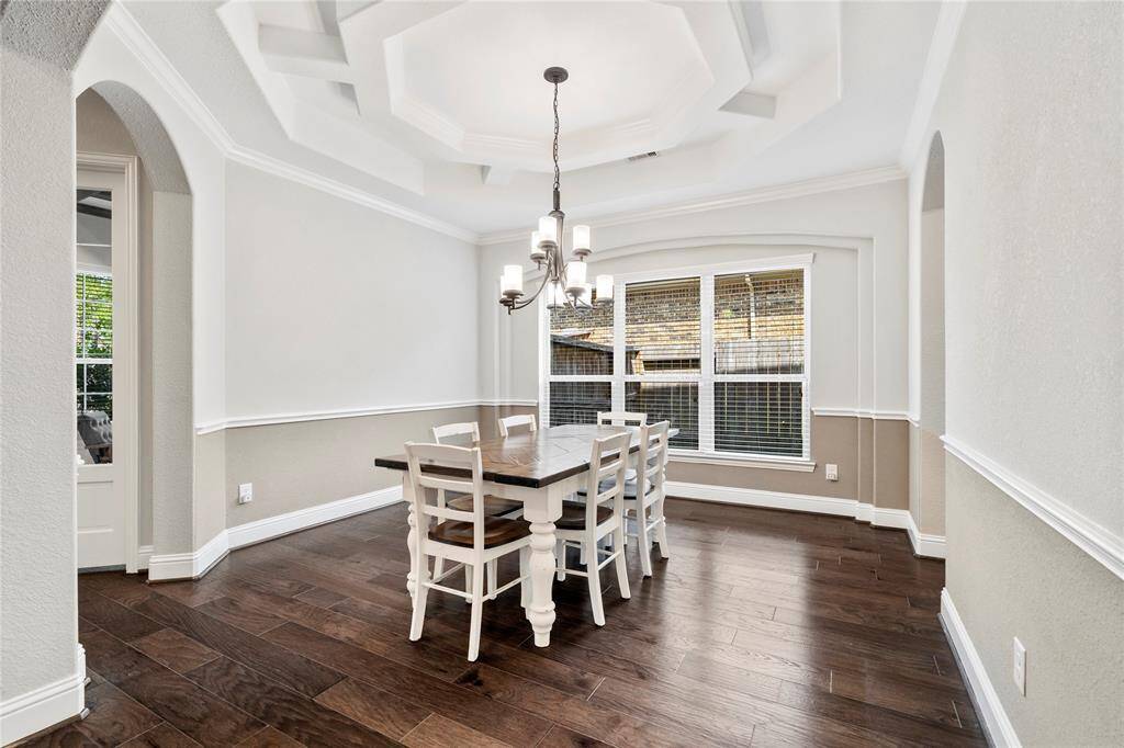 So many details in this dining room with a modern chandelier, large windows providing natural light, elegant tray ceiling, custom trim work and rich hardwood floors. The space is open, inviting, and perfect for family gatherings.