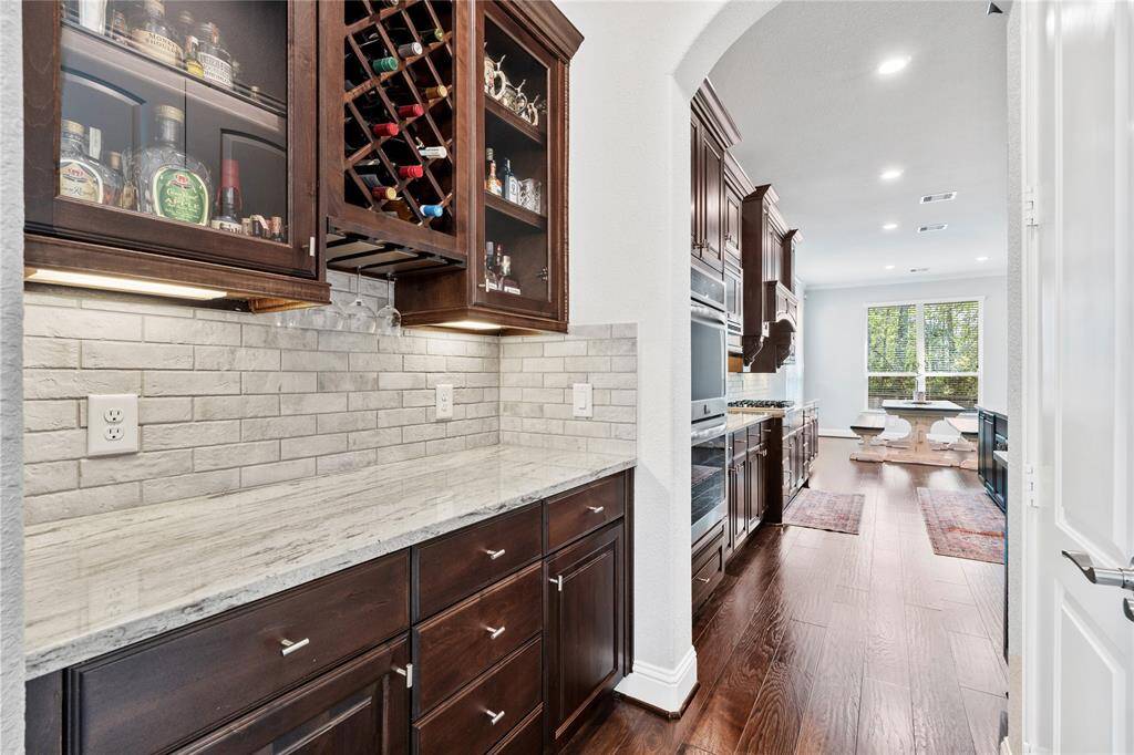 Butlers pantry with plenty of cabinets and a built-in wine rack. The space is well-lit with recessed lighting and has a view into a dining area with large windows.