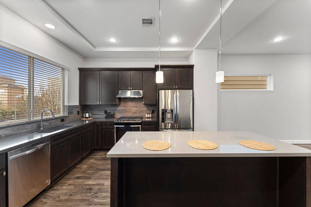 This kitchen features a large central island with pendant lighting. The space is brightened by ample natural light from large windows.