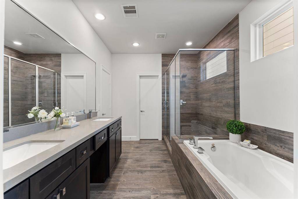 Bathroom features a spacious layout with a large glass-enclosed shower, a deep soaking tub, and dual sinks on a sleek vanity. .