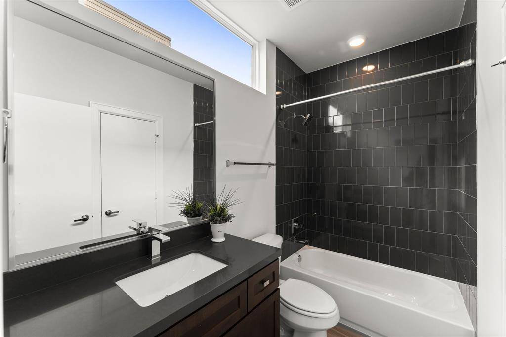 Bathroom features sleek black tile and a stylish vanity with dark countertops. Natural light filters through the window, enhancing the design.