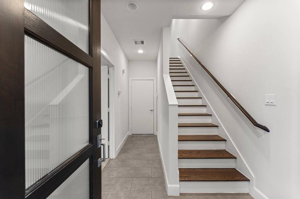 Entryway with a sleek wooden staircase, neutral tile flooring, and freshly painted white walls.