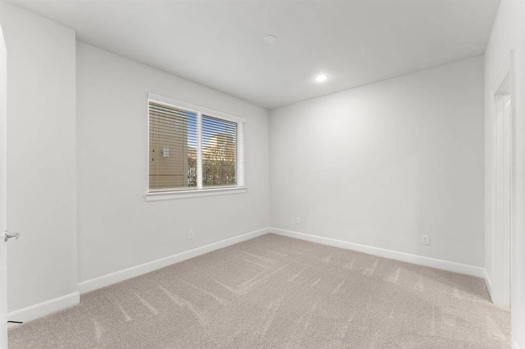 This downstairs room features neutral walls, brand new carpet, a large window with blinds, and recessed lighting, offering a bright, versatile space.