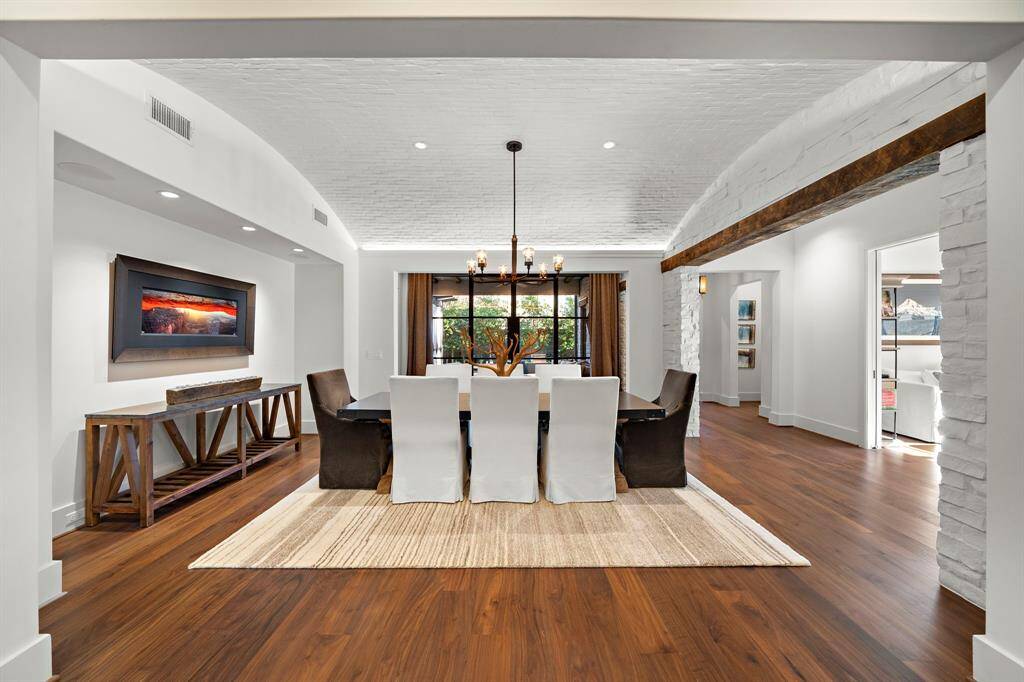 Brick barrel ceiling and rustic beam accents elevate the dining experience, anchored by rich hardwood floors while steel and glass doors frame picturesque views of the yard.