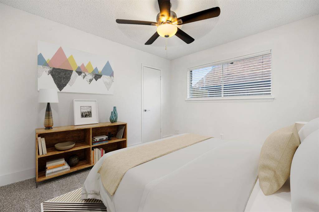 Secondary bedroom features plush carpet, neutral paint, dark stained ceiling fan with lighting and a large window with privacy blinds.