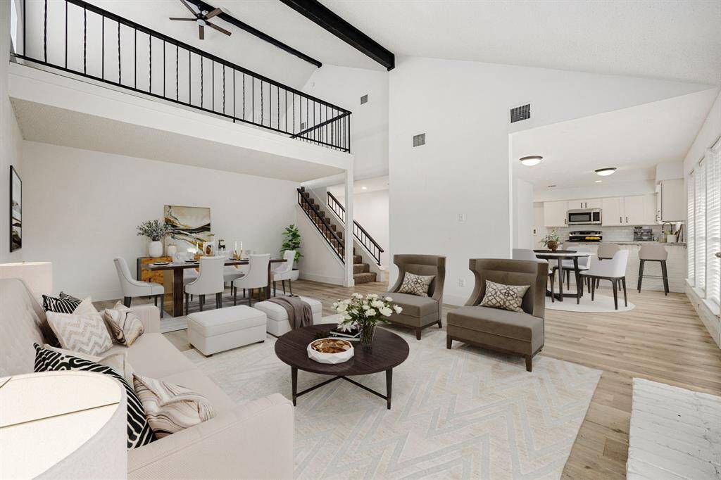 This stunning, light-filled living space boasts soaring ceilings and an open floor plan, providing a seamless flow to the dining and kitchen areas. The expansive layout, abundant natural light, and luxury vinyl plank flooring create an inviting atmosphere, perfect for gatherings and everyday comfort. A staircase leads to a charming gameroom area, enhancing the spacious feel of this beautiful home.