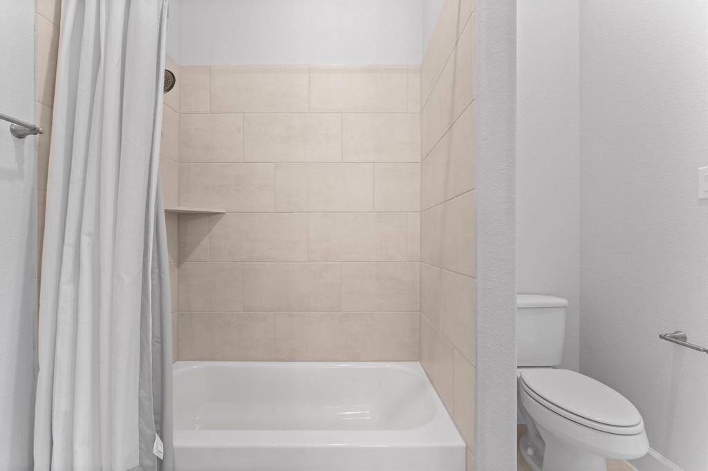 This is a modern, full bathroom featuring a combination bathtub and shower with beige tile surround, a built-in niche for toiletries.