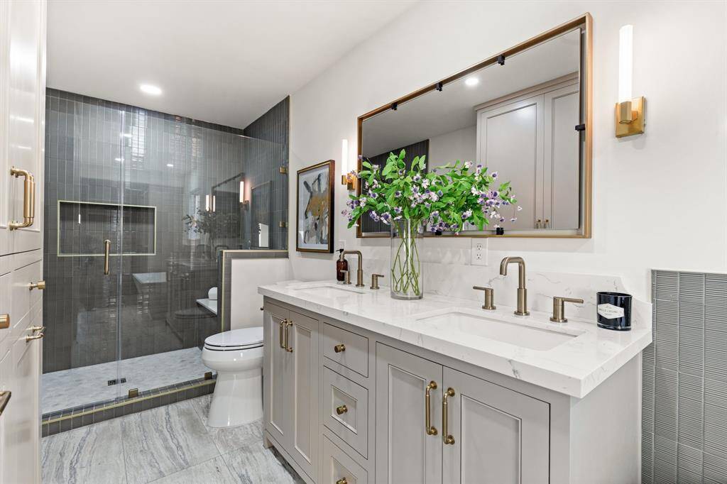The luxurious primary bathroom features contemporary brass hardware, inset cabinetry, dual sinks with quartz countertops, a generous shower, and a freestanding tub.