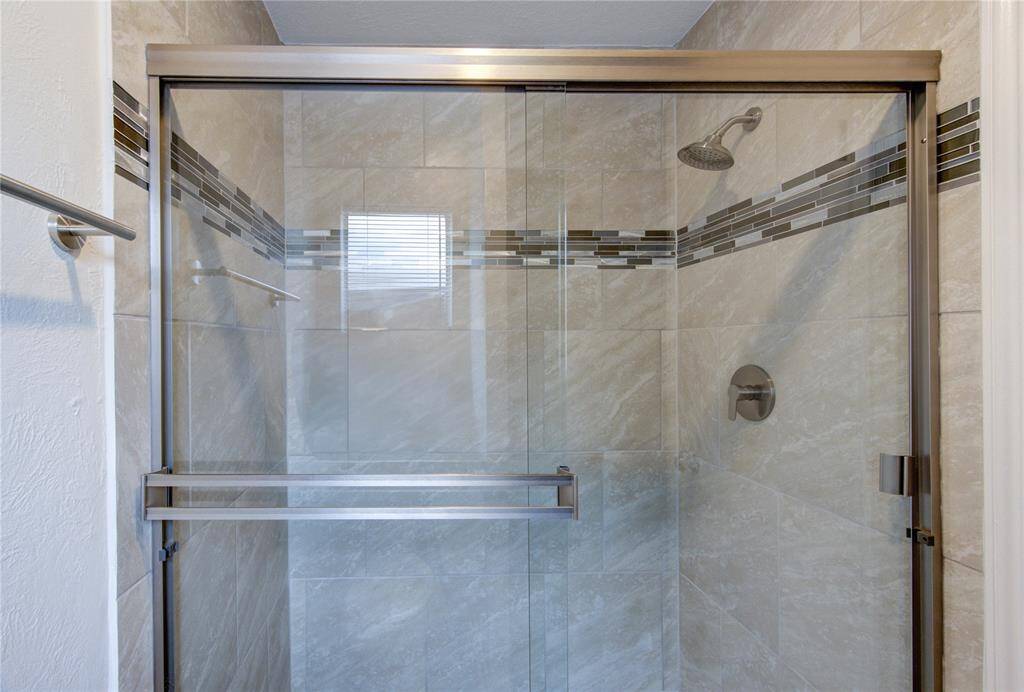 All new primary bath shower with new tile surround with mosaic detail, new valve and faucet, and new shower door.