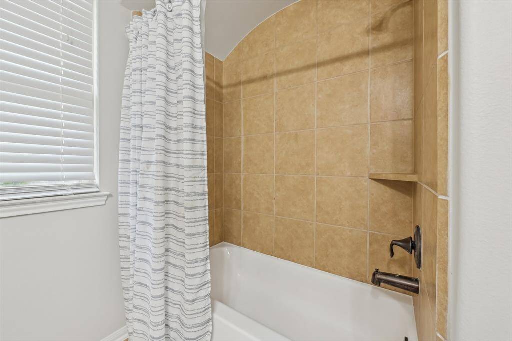 This bathroom features a cozy bathtub with a tiled shower surround in warm tones, complemented by a nearby window with blinds for natural light.  Bathroom 3.
