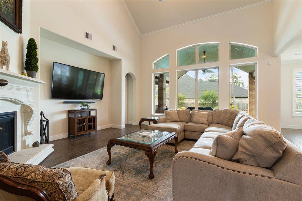 This spacious living room features high ceilings, a cozy fireplace, and large windows that provide ample natural light. The wall of windows opens to a view of the backyard. Ideal for relaxation and entertaining.