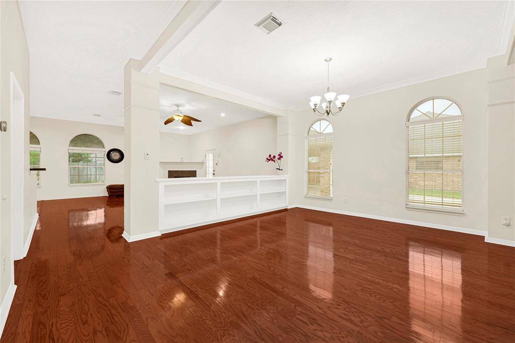 Bright, open-concept dining space with rich hardwood floors and high ceilings. Features large arched windows for natural light, a ceiling fan, and a chandelier. Ideal for comfortable living and entertaining.