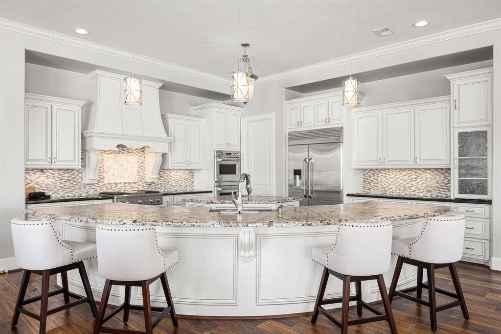 A curved island elevates the luxe space & provides ample seating to accommodate your guests. Organization is key to a well-run kitchen & with dual pantry areas, custom cabinetry, built-in amenities & an abundance of prep space, this kitchen ensures you're ready for any type of entertaining or family gathering.