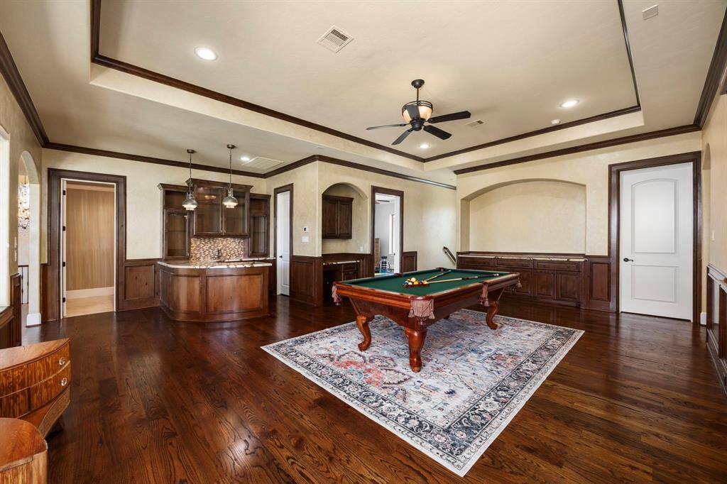 A game room curated for social gatherings that boast an extensive entertainer’s bar, which is an integral part of this room. Hardwood flooring underfoot & walls adorned with custom millwork in rich wood tones add a luxurious warmth to the ambience.