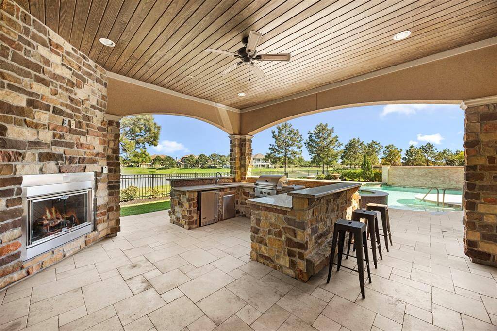 A Summer kitchen perfectly designed with a wrap-around stone bar for entertaining. Fully equipped with a gas grill, 2 burner cooking station, fridge, sink & ample counter space. The fireplace creates a space for intimate gatherings poolside.