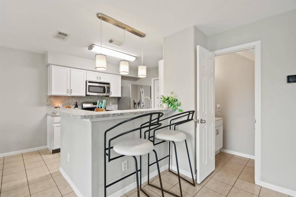 Now into the kitchen. Features include easy care countertops paired with a coordinating backsplash, stainless steel appliances, crisp white cabinets with updated hardware, tons of lighting, and an island with breakfast bar seating.