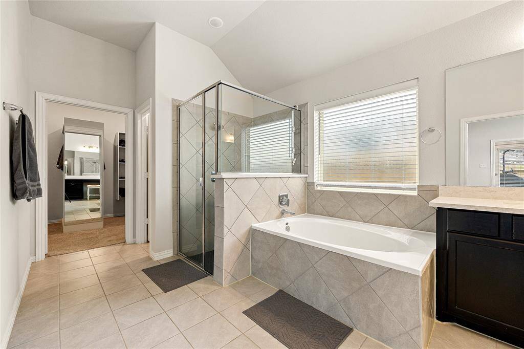 This primary bathroom is definitely move-in ready! Featuring a dark framed walk-in shower with tile surround, separate garden tub for soaking after a long day with custom tile detailing, dark stained cabinets with light countertops, spacious walk-in closet with shelving, high ceilings, custom paint, sleek and dark modern finishes.