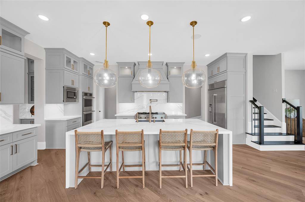 A gourmet kitchen with luxurious finishes, featuring a large island, a Jenn-Air refrigerator, and an additional staircase to the second level.