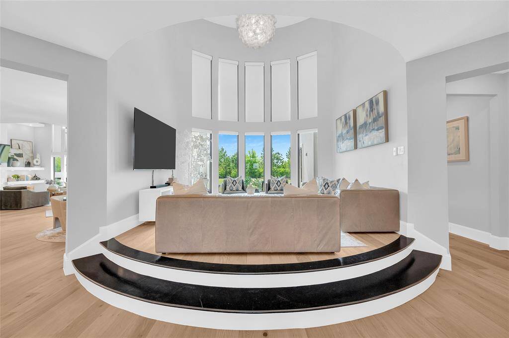 The elevated 2-story living room features a custom chandelier and a stunning wall of windows overlooking the serene backyard.