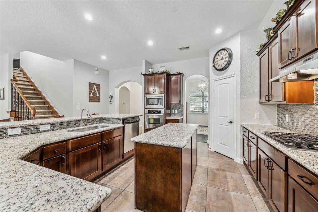 This modern kitchen features elegant granite countertops, dark wood cabinetry, and stainless-steel appliances. It includes a central island for additional workspace and seating. The open layout provides a seamless flow to adjacent living spaces. Perfect for cooking and entertaining