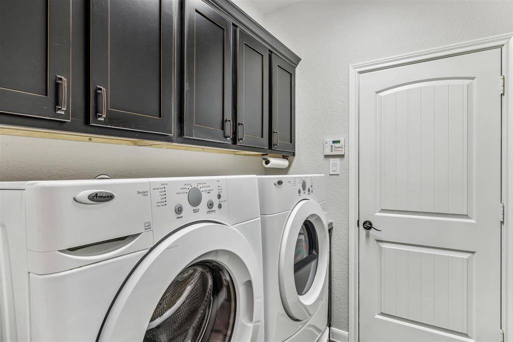 Well-equipped laundry room with a washer and dryer, cabinetry for storage, and a door with access into the attached two car garage. The space is functional and organized, ideal for managing laundry needs
