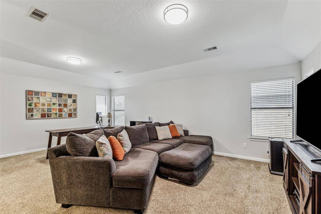 This photo showcases a spacious second floor game room with soft carpeting. The room is bright with ample natural light from windows and features modern ceiling light