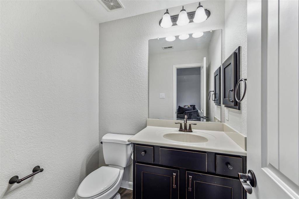 Second floor powder room conveniently located next to the game room featuring a sleek vanity with dark cabinetry, a white countertop, and a polished faucet. It includes a large mirror, and contemporary light fixtures all set against neutral walls
