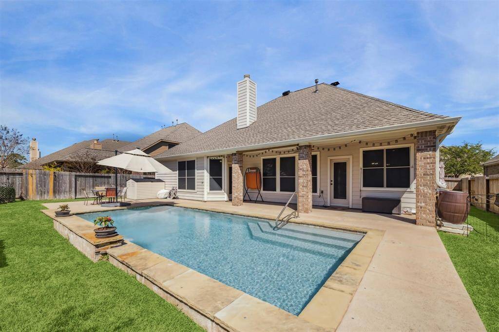 Additional view of the charming backyard featuring a spacious in-ground pool with a surrounding patio, perfect for relaxation and entertainment. The home exterior has a brick facade with a covered patio area, providing shade and comfort