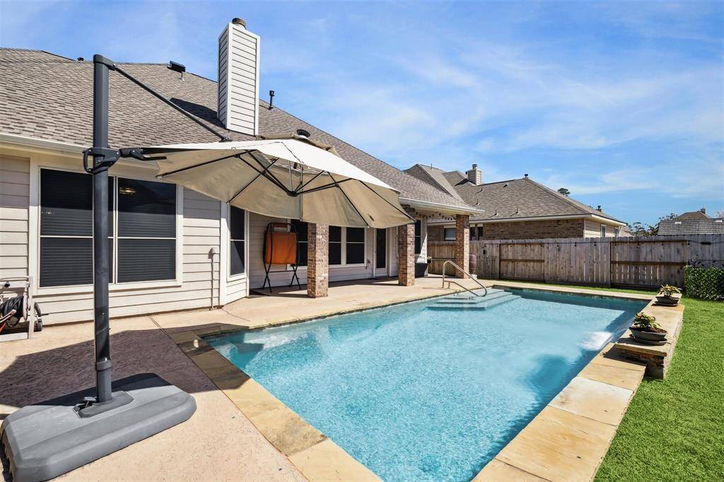 Alternate view of the pool surrounded by a paved area and a grassy lawn. Solar window screens added (2023) to keep the home even more efficient