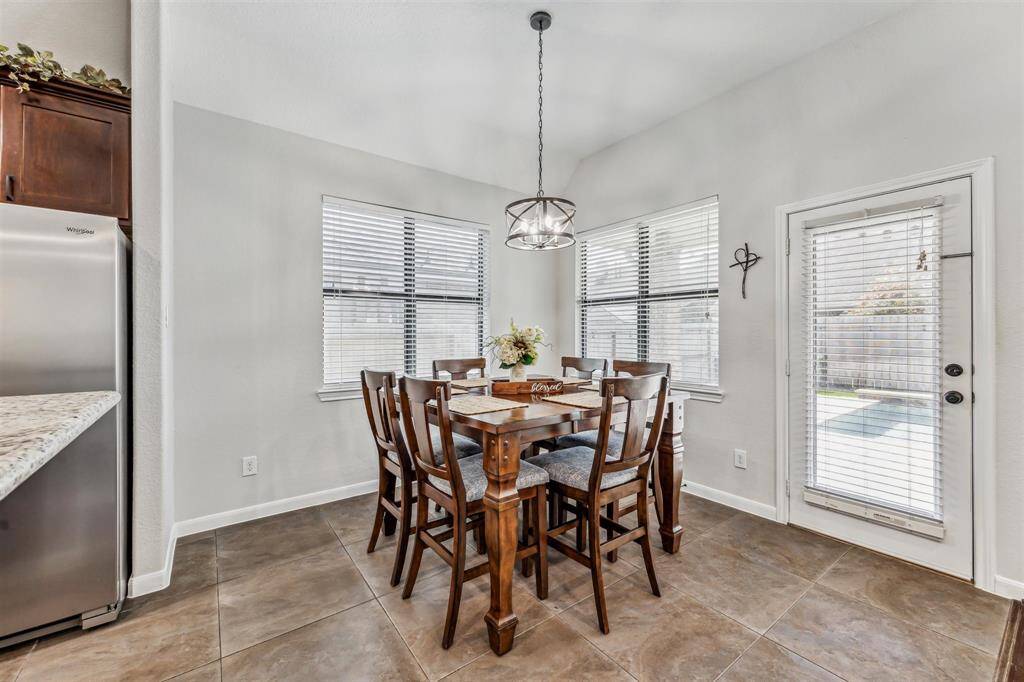 Bright and inviting dining area with large windows, and a modern light fixture. The space features tiled flooring and offers easy access to the outdoor patio through a glass door