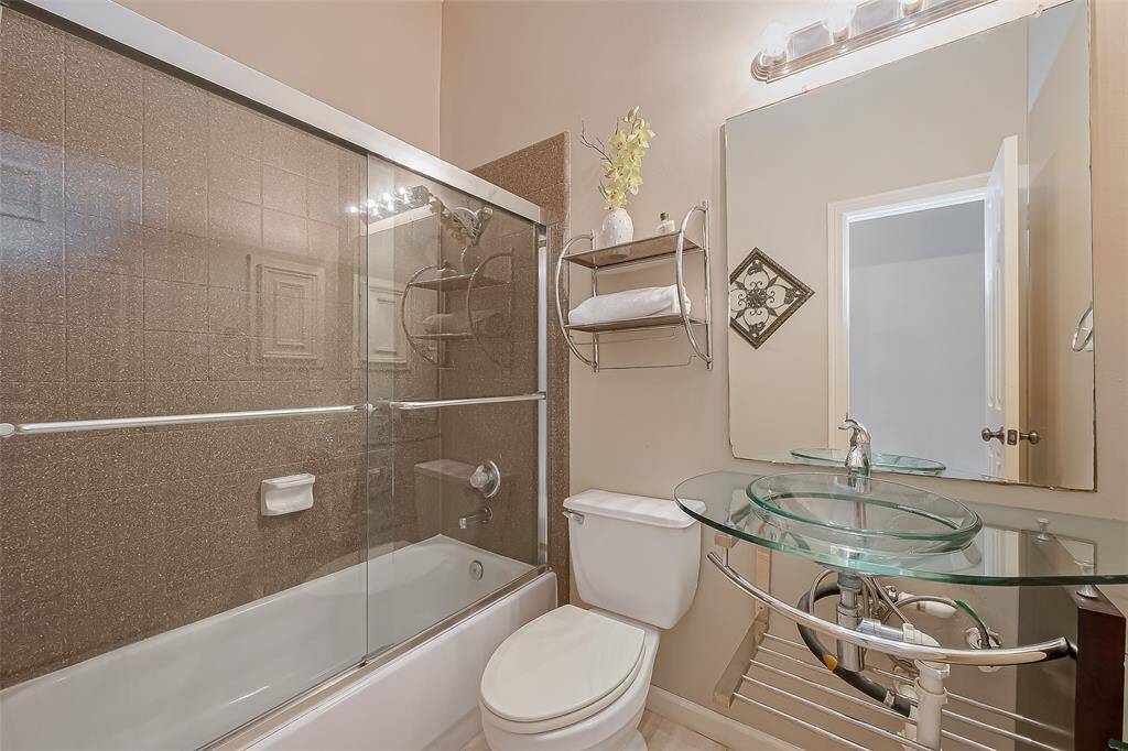 Second full bath with clear glass vessel sink and shelving