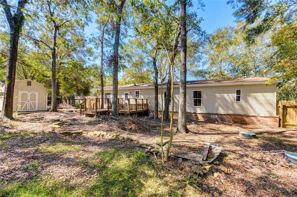 This is a single-story home nestled among mature trees, featuring a spacious deck and a matching storage shed in the backyard. The home presents a serene, natural setting with ample outdoor space for recreation and relaxation.
