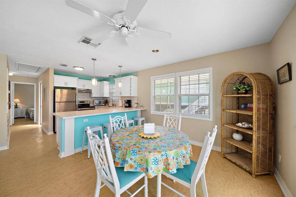 This open dining area flows seamlessly into the kitchen, showcasing a cheerful and coastal-inspired atmosphere. Double windows and a ceiling fan enhance the light and breezy feel.