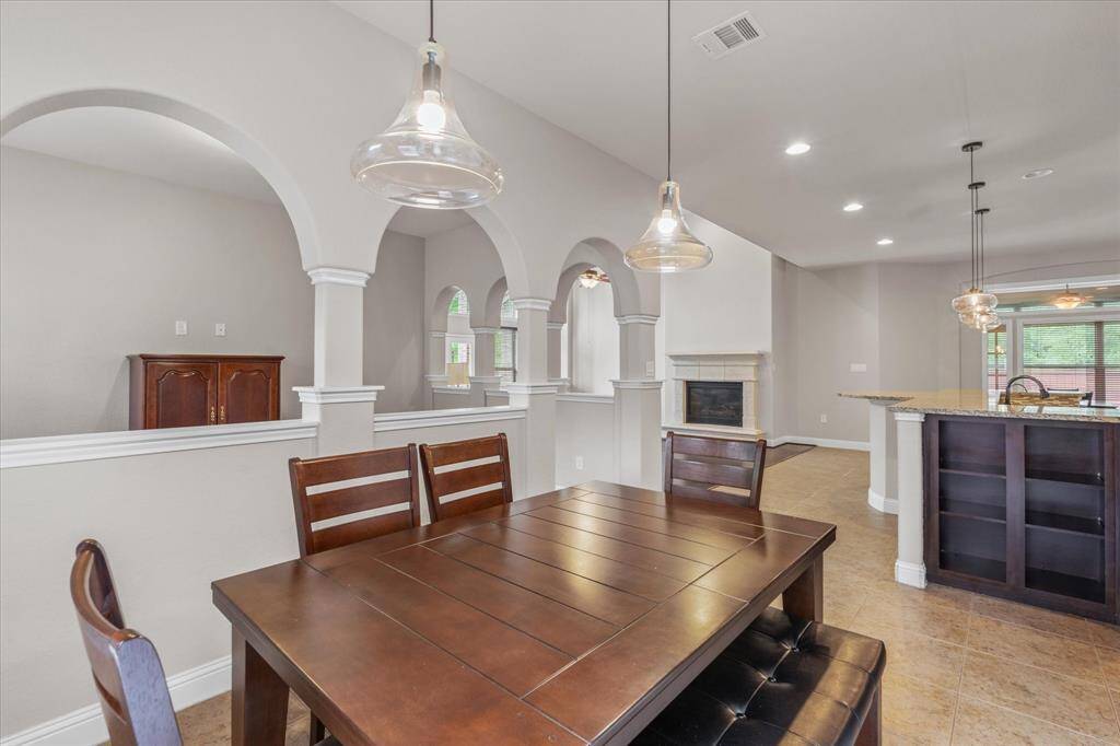 This photo showcases a spacious dining area with elegant arches and pendant lighting, seamlessly connecting to an open-plan kitchen and living space with a fireplace. The neutral tones and tiled flooring create a warm and inviting atmosphere.