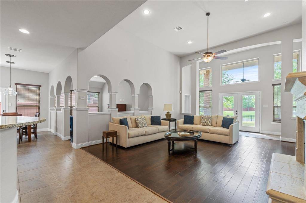 Spacious living room with high ceilings, natural light, and wood flooring. Features a cozy seating area, fireplace, and large windows overlooking the backyard. Open layout connects to the kitchen and dining area. Perfect for entertaining.