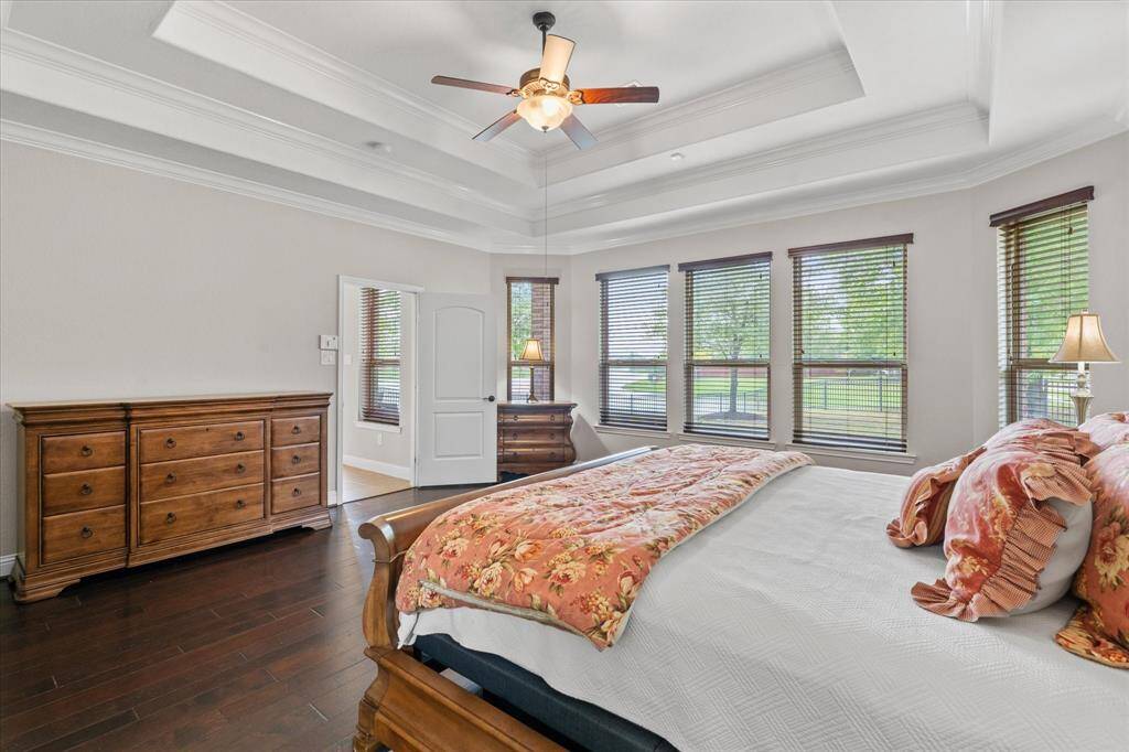 This spacious  bedroom features a tray ceiling, hardwood floors, and abundant natural light from multiple large windows.