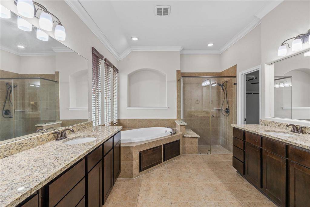 This spacious bathroom features a double vanity with granite countertops, a large soaking tub, and a separate glass-enclosed shower. The room is well-lit with modern fixtures and offers ample storage within its elegant cabinetry.