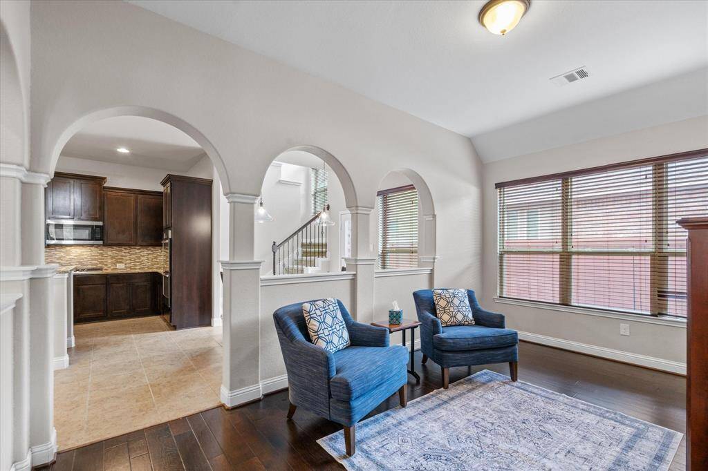 This inviting living space features rich wood flooring, and large windows for ample natural light. Arched openings lead to the kitchen, which boasts dark wood cabinetry and stone tile flooring, creating a warm and elegant atmosphere.