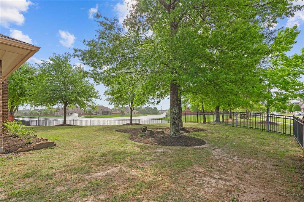 Spacious backyard with lush trees and a view of a serene lake, enclosed by a charming black fence. Ideal for outdoor relaxation and enjoying nature.