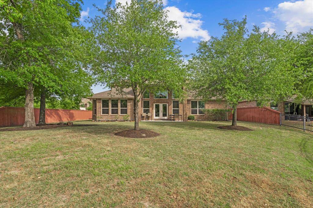 This photo shows a spacious backyard with a well-maintained lawn and mature trees, providing a serene and private outdoor space. The house features a brick exterior with large windows and a patio area, perfect for relaxation and outdoor activities.
