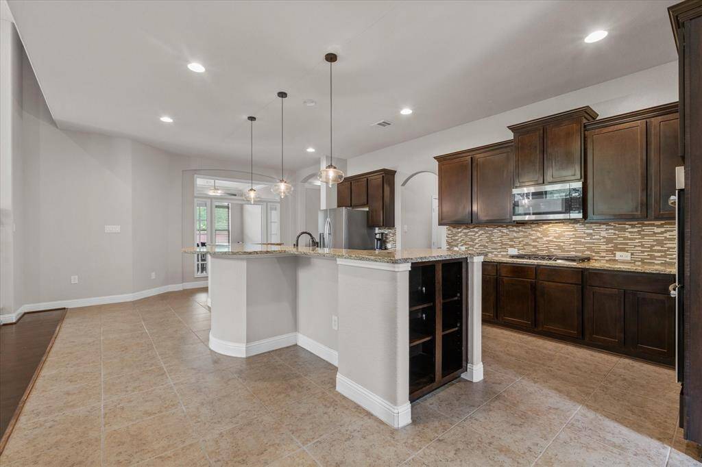 This modern kitchen features dark wood cabinetry, a stylish tile backsplash, and a spacious island with pendant lighting. The open layout connects to the dining area, perfect for entertaining.