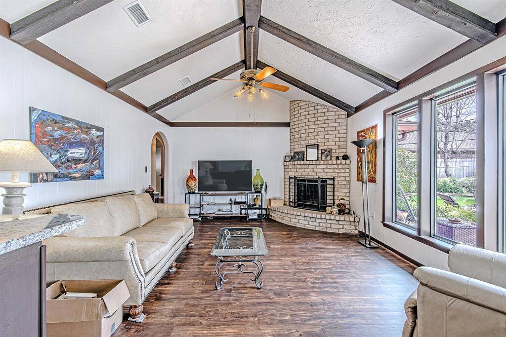 Stunning 12 ft vaulted ceilings with exposed beams complement the brick fireplace and arched doorway, adding architectural charm to this spacious living area.