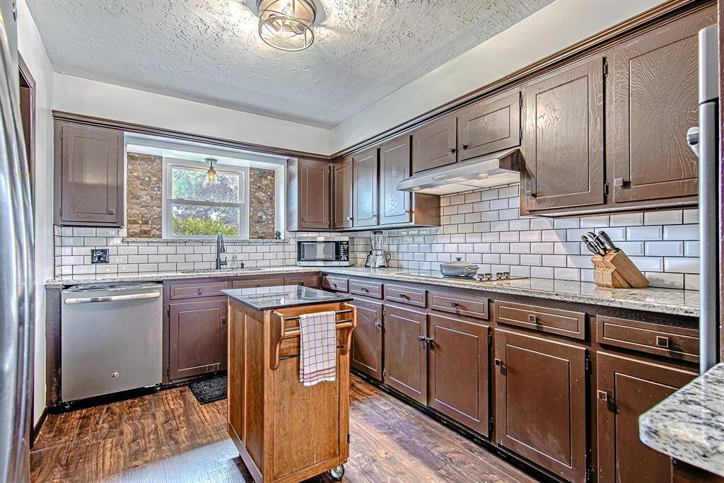 Charming kitchen with rich wood cabinetry, granite countertops, and a subway tile backsplash, offering a view of the front yard through the sunny window.