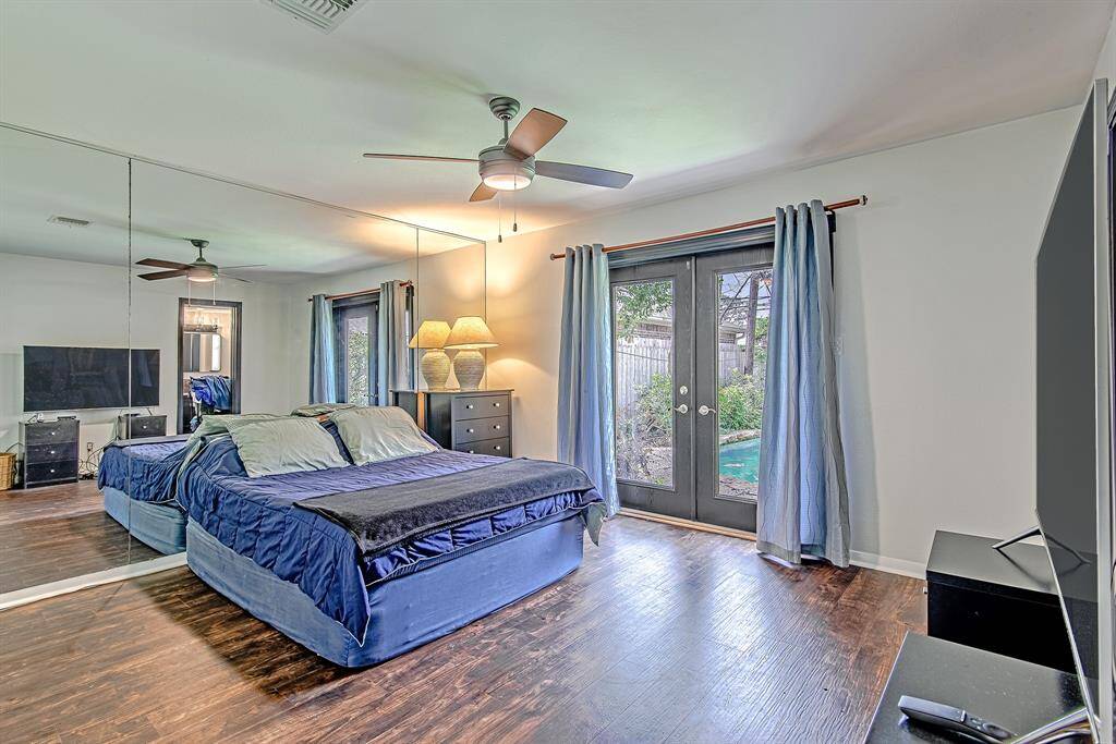 Spacious primary bedroom features a mirrored wall and elegant French doors that open directly to the pool area, offering a private retreat with outdoor access.