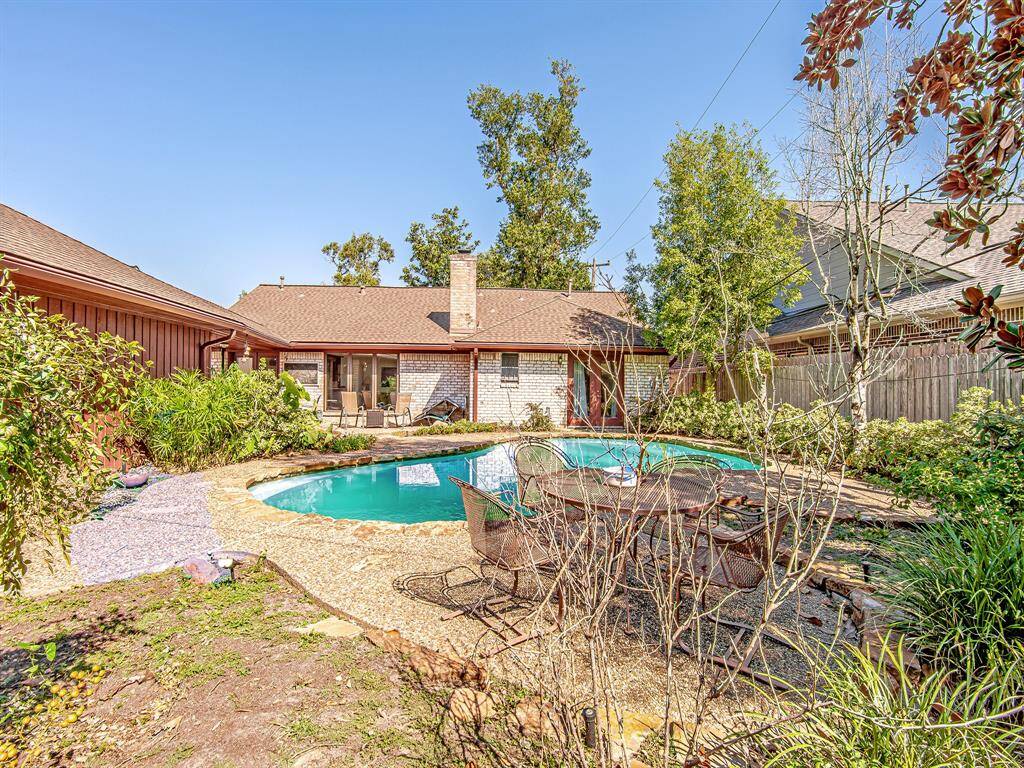 Another angle of the backyard showcases the beautifully curved pool design and well-maintained greenery, creating a peaceful outdoor escape with multiple seating areas.