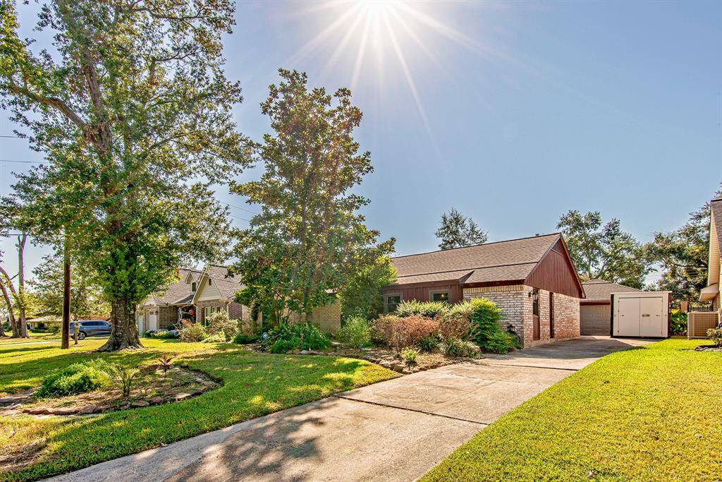 Charming front elevation with a long driveway leading to the garage, surrounded by mature trees and well-maintained landscaping for added curb appeal.