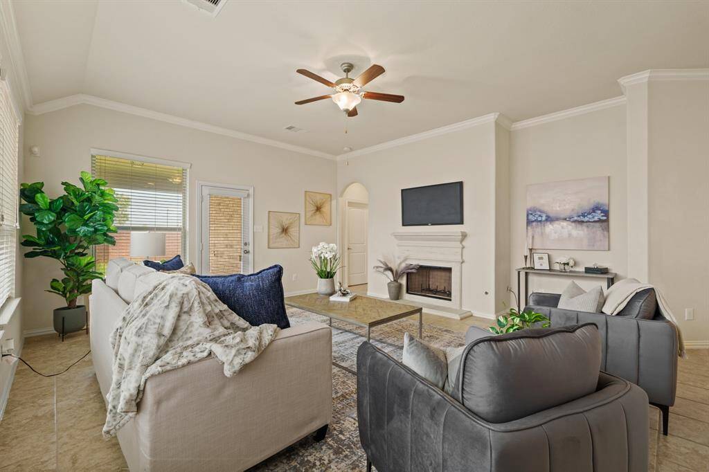 This spacious family room showcases soft neutral finishes, including tile flooring, neutral paint, a raised ceiling with crown molding and a lit fan, a romantic wood-burning fireplace, and plenty of room to relax and unwind.
