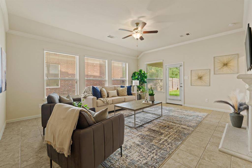 Flooded with natural light, this spacious family room features a wall of windows and a glass patio door that brighten the space throughout the day. Neutral tile flooring, soft paint tones, a raised ceiling with crown molding and a lit fan, and a romantic wood-burning fireplace all come together to create a warm and welcoming place to relax and unwind or entertain friends and family.