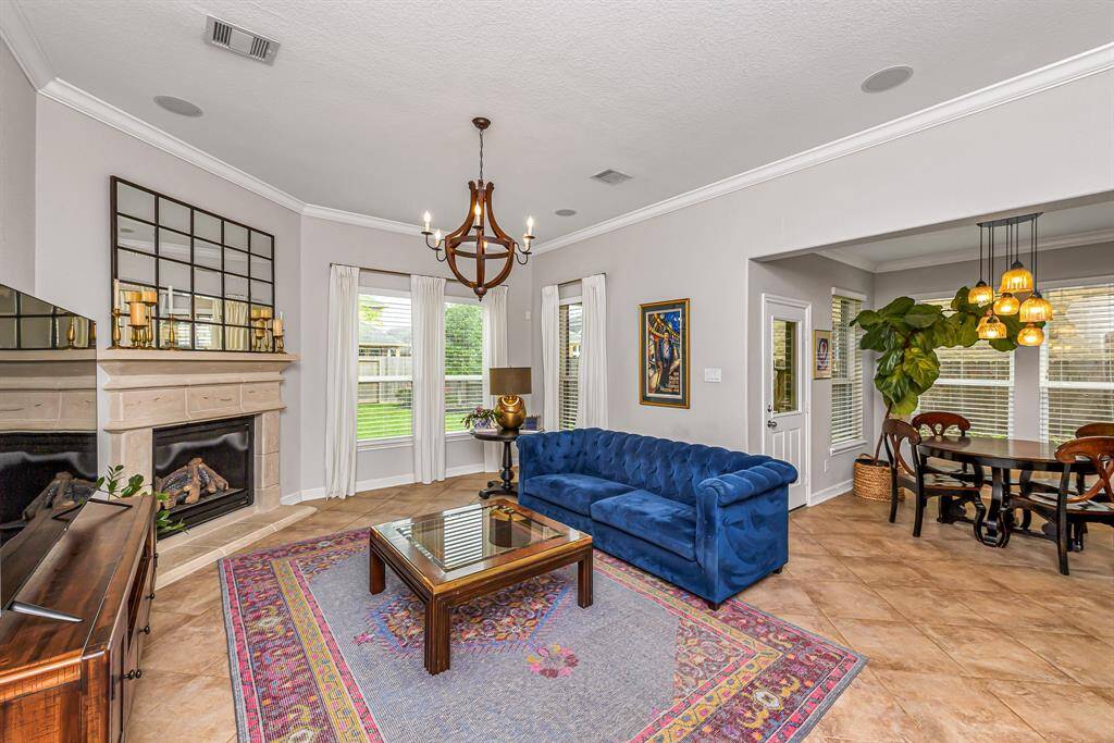 The family room features gorgeous tile flooring, high ceiling with crown molding, and a fireplace with mantel as a cozy focal point. Windows with custom blinds let in natural light and provide views of the backyard.