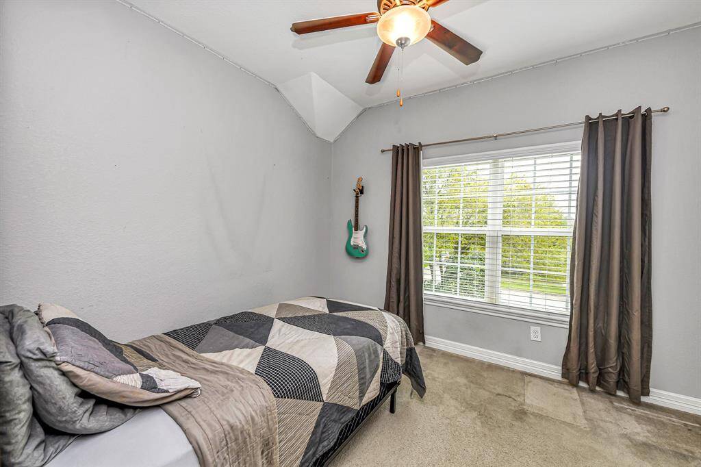 Cozy secondary bedroom with neutral carpet, vaulted ceiling, and a large window with custom blinds that brings in great natural light. Perfect for guests, kids, or a home office setup.
